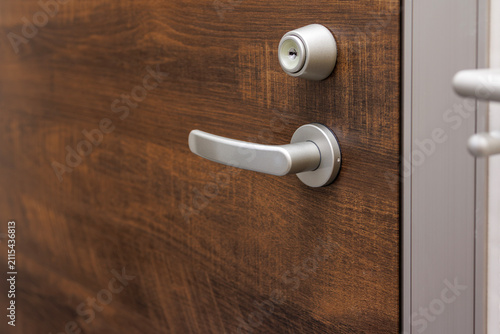 Silver door lever handle and cylinder lock on dark wood door.