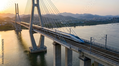 High-speed train crossing a modern cable-stayed bridge over a wide river at sunset.