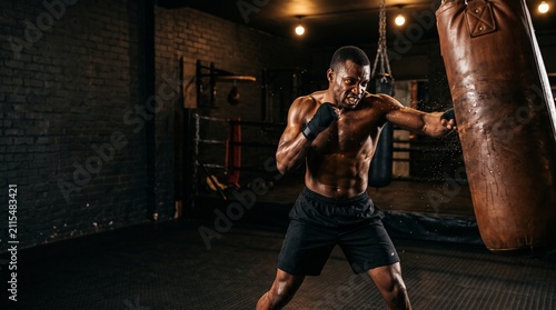 Intense Training Session: A muscular man is engaged in a vigorous boxing training session, punching a heavy bag with focus and determination.