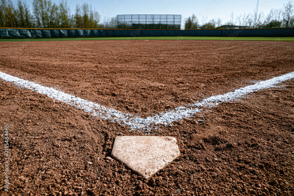 Fototapeta premium Baseball diamond viewed from home plate, empty field with bleachers and trees in the background on a clear day.