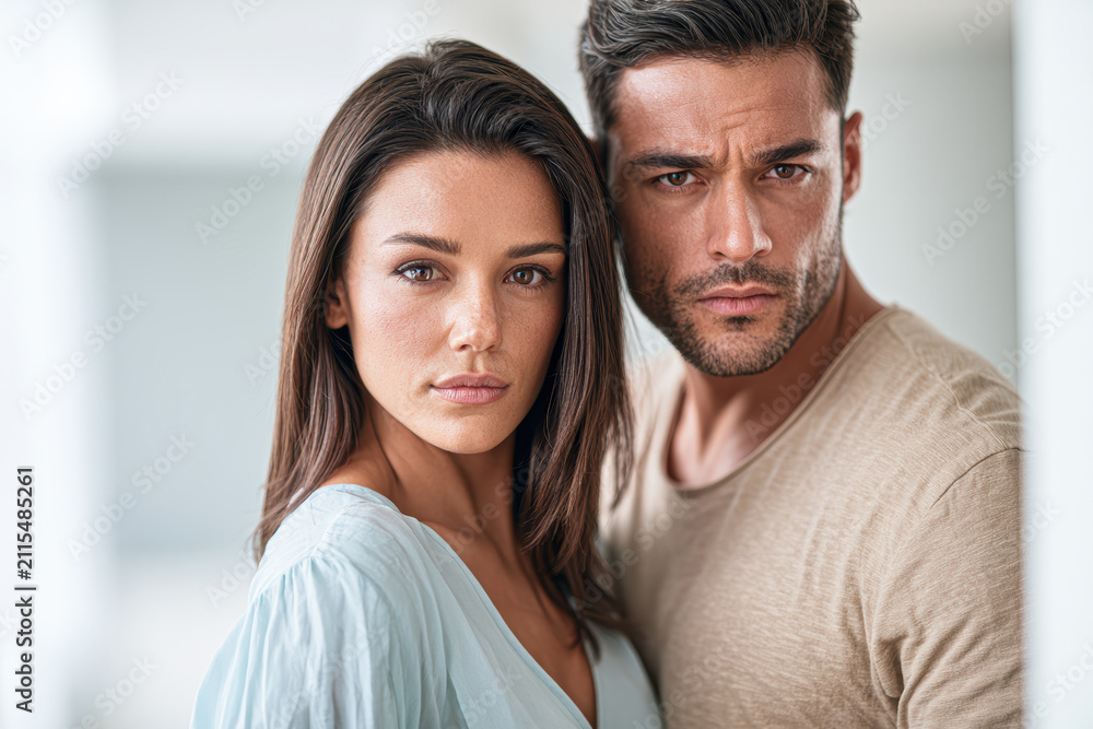 Fototapeta premium Close-up portrait of a serious young man and woman standing side by side indoors, both looking directly at the camera with intense expressions.