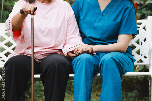 Canvastavla Smiling elderly lady holding hands with young female nurse in uniform outdoors