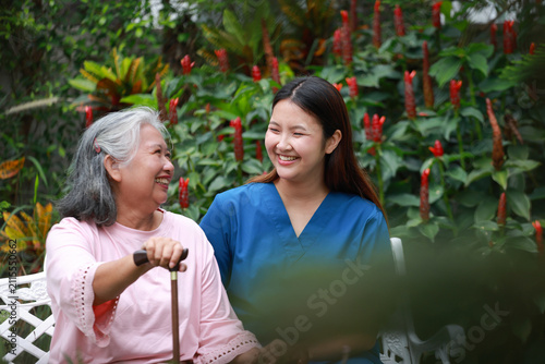 Canvastavla Professional healthcare worker sitting beside an elderly woman outdoors, offering emotional support and attentive senior care in a peaceful garden setting with natural light