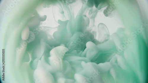 Watercolor pigment blooms through clear water as soft sage green and ivory hues unfurl into organic cloudlike formations under gentle overhead lighting with elegant cinematic macro motion.