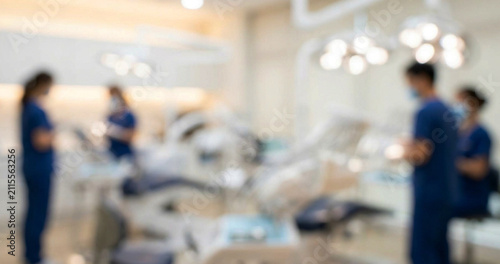 A blurred image depicting a dental clinic with dental professionals in blue scrubs working. The modern environment features dental equipment and bright lighting.