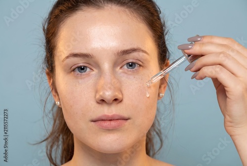 Young woman applying facial serum with glass dropper