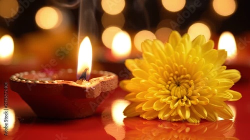 Traditional clay diya lamp with a burning flame and smoke next to a yellow chrysanthemum flower for diwali festival