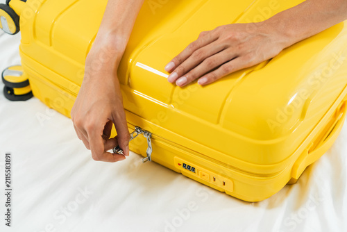 A woman's hands are zipping up a yellow wheeled suitcase after she's finished packing for her trip.
