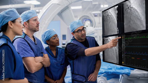 Medical team of cardiologists reviewing coronary angiogram and heart monitoring screens in a catheterization lab