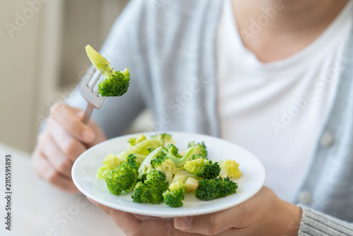Bild auf Leinwand Close up of a woman hand holding fork with green broccoli over a white plate for