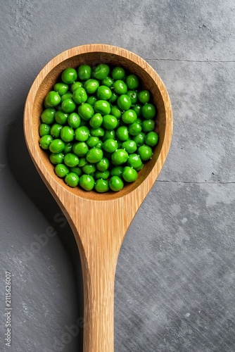 A wooden spoon filled with green peas on a gray surface