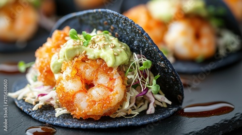 Fusion tacos with crispy tempura shrimp, creamy avocado sauce, microgreens and sesame seeds on premium blue corn tortilla served on dark slate