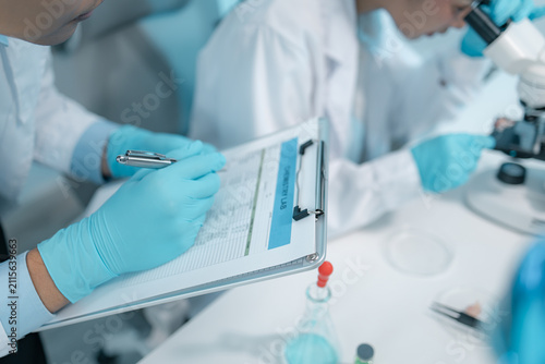 Obraz na płótnie Biomedical scientists perform laboratory experiments using microscopes, laboratory glassware, and biological samples while recording results to support medical research, diagnostics and biotechnology