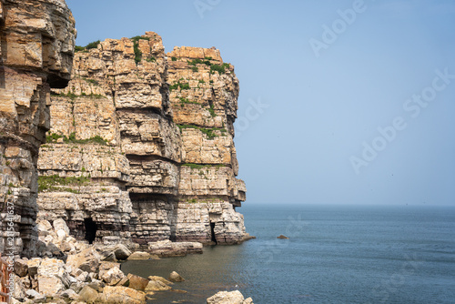 Fotografía Layered Coastal Cliffs Meeting Calm Blue Sea Under Clear Sky
