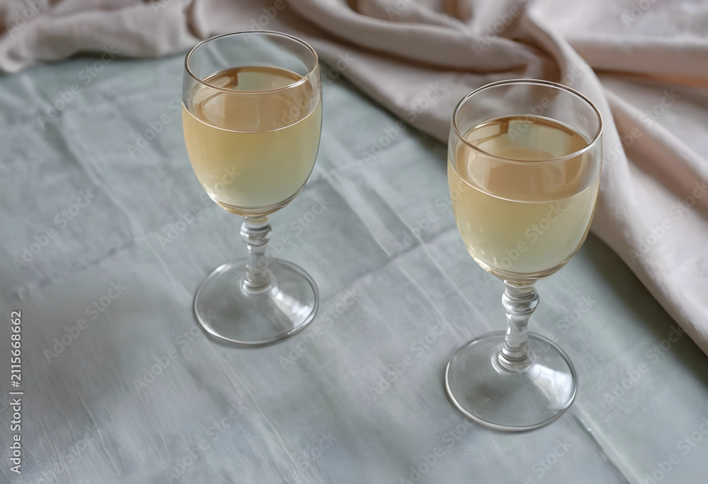Obraz premium Two glasses of white wine on a light green tablecloth with a beige napkin, elegant beverage and dining concept, this arrangement suggests an elegant dining experience or a celebratory event
