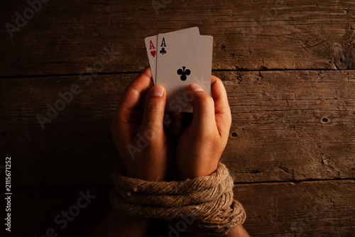 Bild auf Leinwand Hands tied with rope holding playing cards on a wooden table.