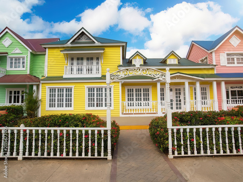 Vibrant Dominican street with colorful Caribbean houses, palm trees, and flowers under a bright blue sky. Ideal for travel, vacation, and tropical themes.