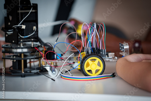Robotics Project Close-Up of a Wheeled Educational Robot with Exposed Circuit Boards, Sensors, Motors, and Colorful Jumper Wires Beside a Robotic Arm