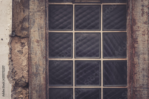 Window with grid pattern and weathered frame in an old building during daylight