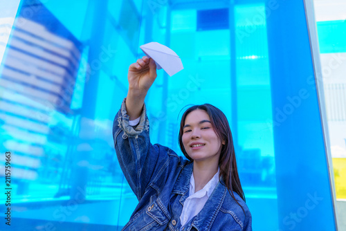 Obraz na plátně Young Asian girl holding paper airplane, winking at camera, expressing freedom,