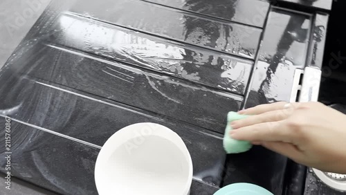 Top view close up of a hand scrubbing a black kitchen sink with a green sponge