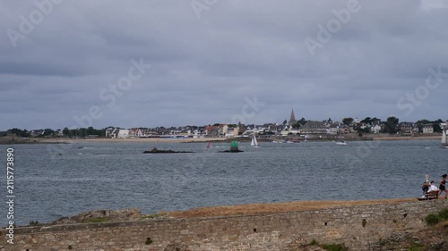 Coastal town seen across water, boats floating, people relaxing near shore