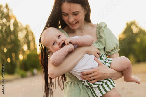 Happy baby held by mother outdoors during golden hour with bokeh background