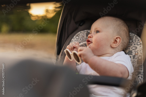 Adorable baby in stroller holding sunglasses, enjoying outdoor sunset light