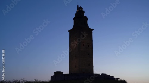 Detalle nocturno del faro de la Torre de Hércules iluminado, destacando sobre el cielo oscuro y el paisaje costero de A Coruña.
