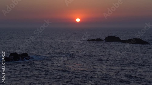 Atardecer atlántico desde la costa de A Coruña, con el sol naranja a punto de ponerse sobre el horizonte y tiñendo el mar de tonos cálidos.