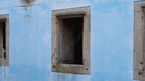 Detalle de una ventana de una casa abandonada en el casco antiguo de Lugo, con fachada azul envejecida y puertas de madera abiertas que acentúan su aspecto decadente.