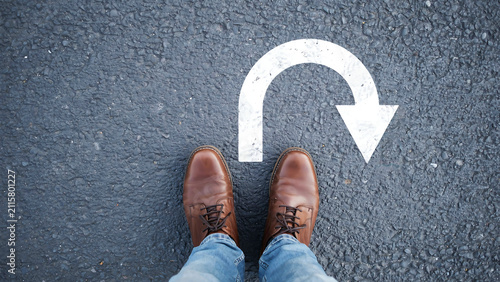 Person standing on asphalt road looking at white u-turn arrow symbol with direction decision lifestyle navigation standing pavement opportunity strategy