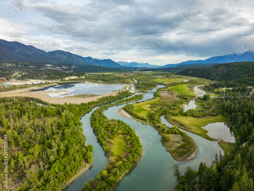 Aerial view of Radium Wetlands Recreation Site featuring a winding river through lush meadows and forests with distant mountains, East Kootenay, British Columbia, Canada.