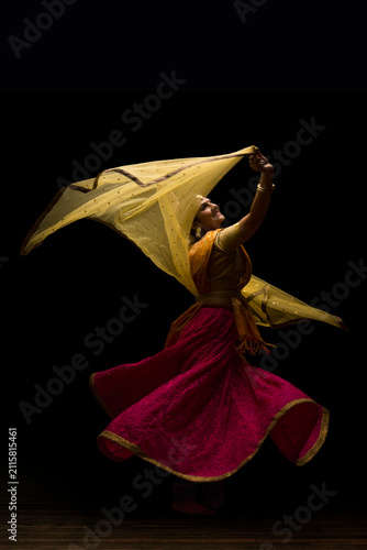 Kathak dancer circling gracefully during a performance in front of a dark background. 