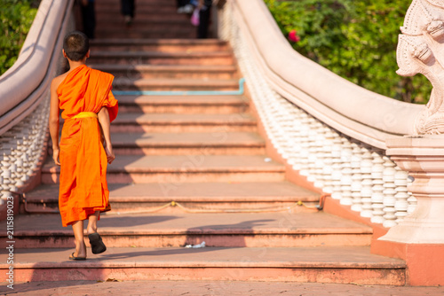 Photography Young Buddhist novice monk walking up temple stairs in bright orange robe