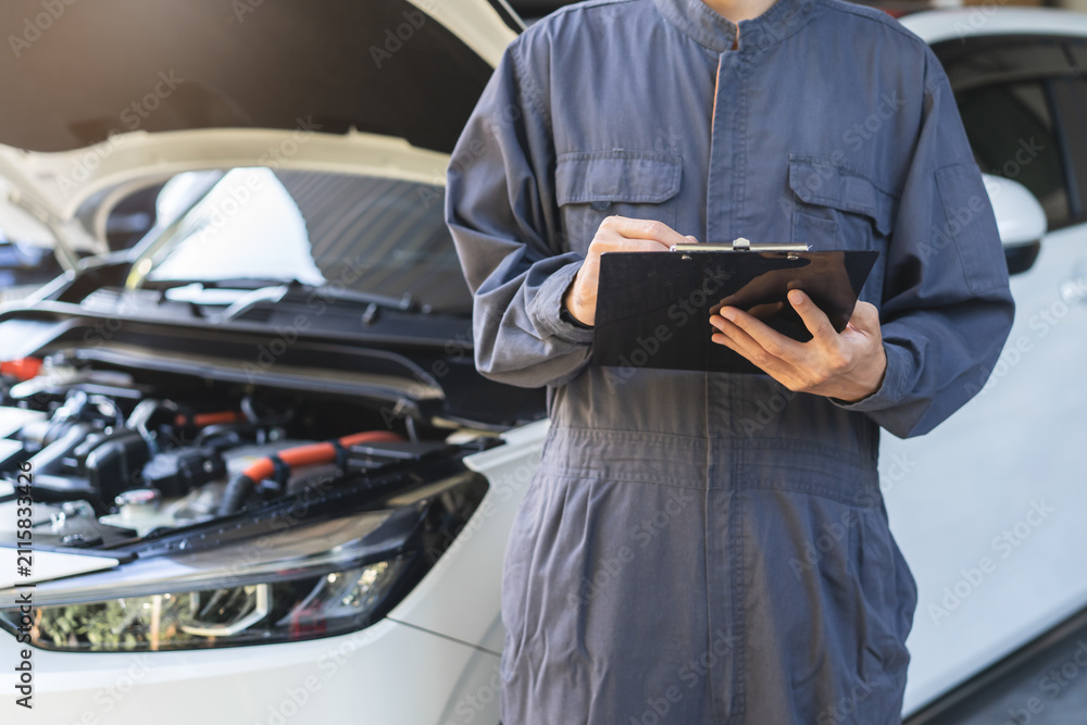 Fototapeta premium Auto check up and car service shop concept. Mechanic writing job checklist to clipboard to estimate repair quotation to client at workshop garage.