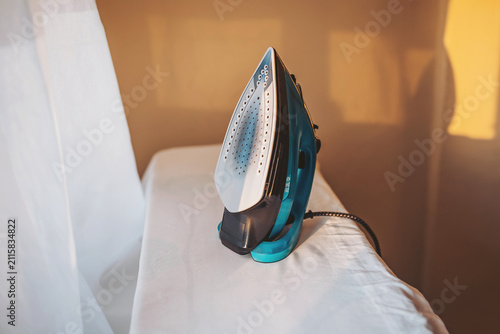 Принти на полотні Iron rests on a crisp white cloth in warm sunlight, ready for a day of smoothing