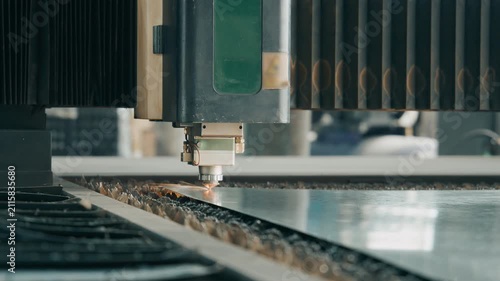 Close up of laser cutting machine incising metal sheet with sparks in workshop