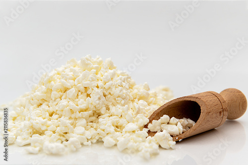 White crumbly cottage cheese with a wooden scoop on a white background.