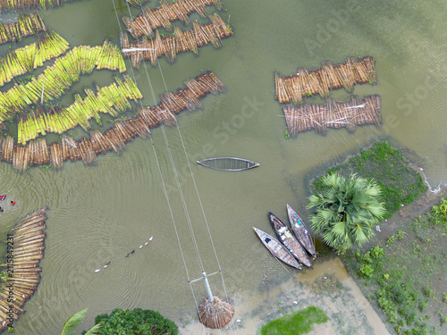 Aerial view of Patul with jute plants soaking in water for the retting process alongside traditional wooden boats and a power line pole in Natore District, Rajshahi Division, Bangladesh.