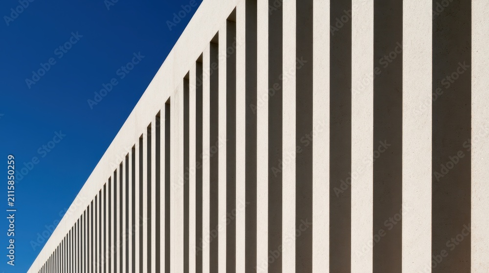 Obraz premium Minimalist modern architecture with repeating concrete columns and dramatic shadows against a deep blue sky