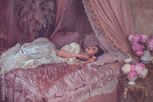 Foto Sensual dark-haired lady posing on a velvet bed surrounded by blooming pink peon