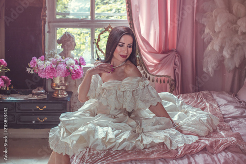 Foto Sensual dark-haired lady posing on a velvet bed surrounded by blooming pink peon