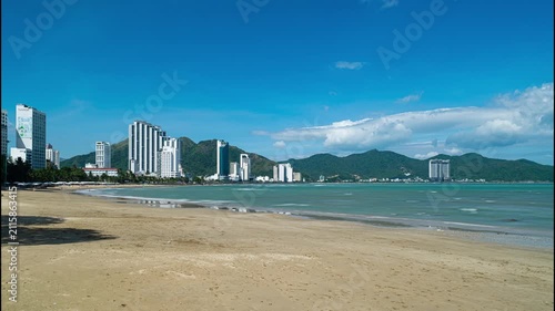Sunny view of Nha Trang beach with modern waterfront buildings, calm sea, blue sky and distant mountains. No people, tropical coastal city in Vietnam.