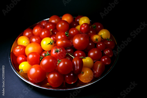 Side view of different types of cherry tomatoes on a silver tray, dark background
