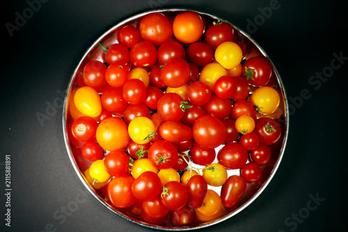 Top view of different types of cherry tomatoes on a silver tray, dark background
