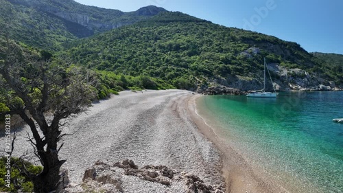 Sveti Ivan beach, pebble cove on Cres Island, Croatia, showing turquoise crystal clear Adriatic sea water, surrounded by green hills, with a sailboat anchored near coastline in Cres Island of Croatia