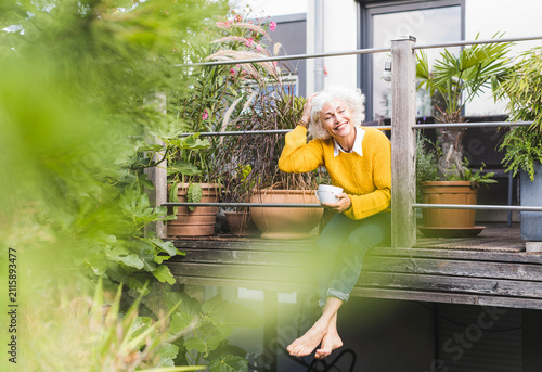 Mature woman with hand in hair sitting at home against railing