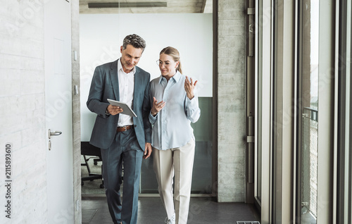 Smiling mature businessman discussing with businesswoman over tablet PC in office