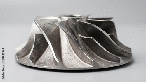 Curved vanes of a stainless steel centrifugal pump impeller on a light grey background